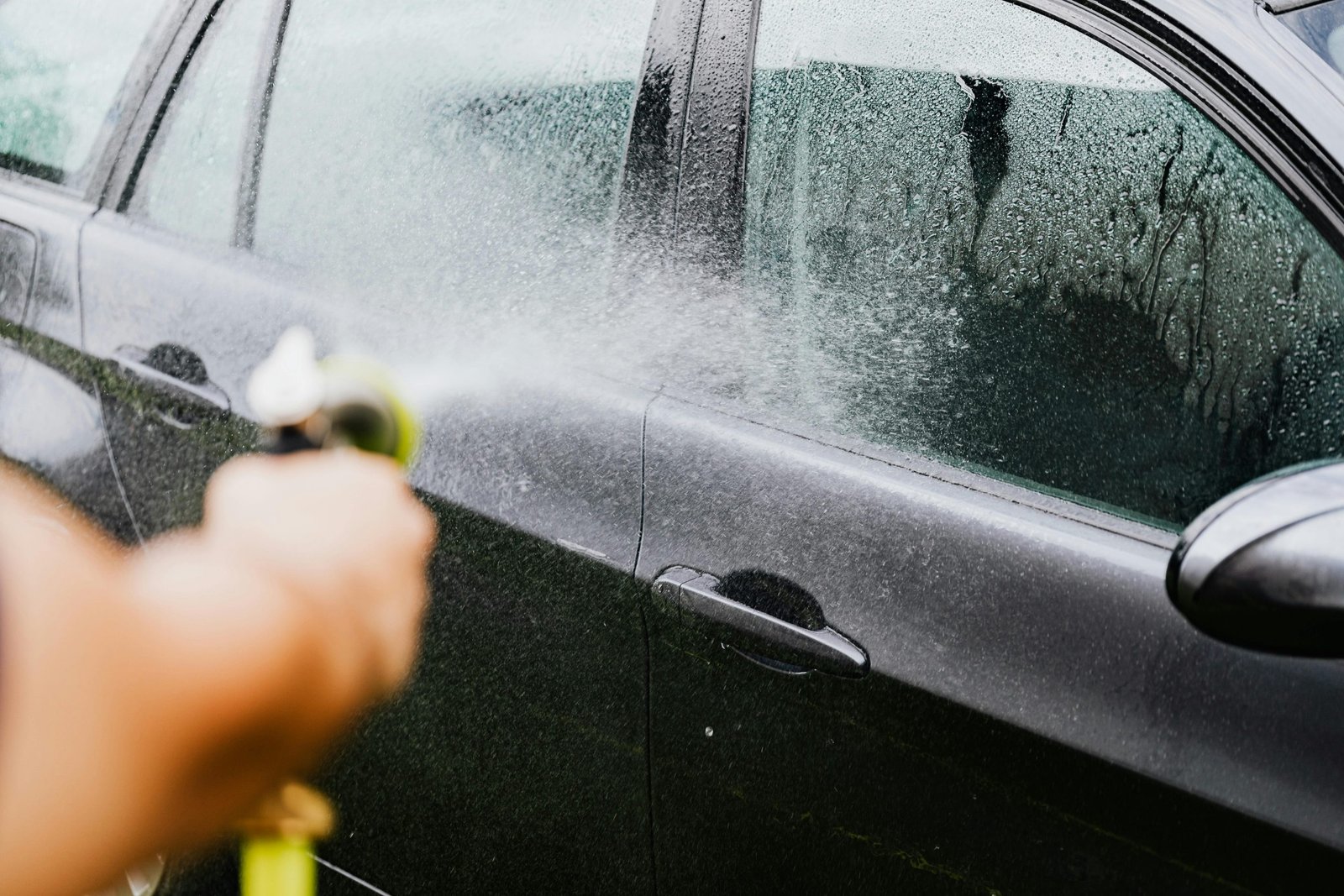 Car Cleaning A car being washed with a hose outdoors. Water sprays create a cleaning effect on the vehicle.